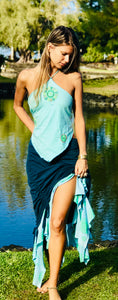 A woman wear a soft cotton lycra two tone skirt that is navy and turquoise. The skirt is adjustable in length with cinch options on 4 sides. She is standing in front of palm trees on a beach in Hawaii.
