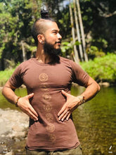 Load image into Gallery viewer, Man is wearing a soft cotton tee shirt with chakra symbols standing in front of palm trees at the water in hawaii