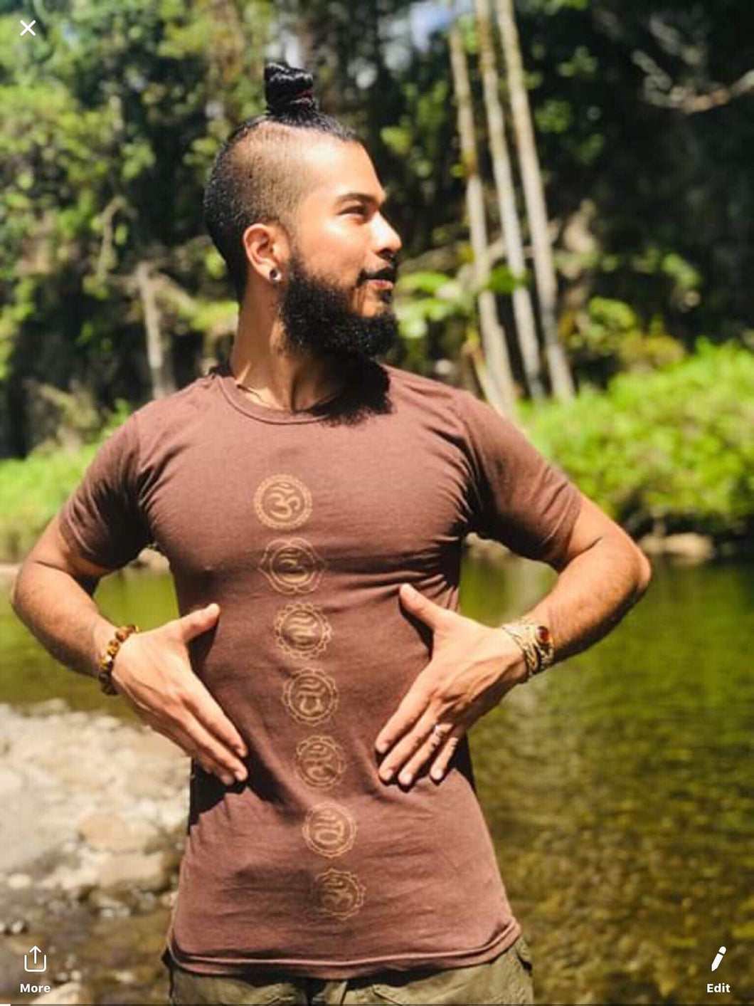 Man is wearing a soft cotton tee shirt with chakra symbols standing in front of palm trees at the water in hawaii